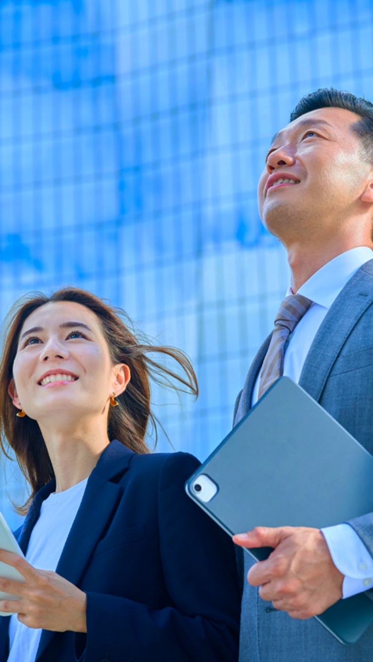 スマホを持った女性とスーツの男性が空を見上げている様子